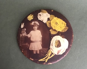 May include: A round, brown, decorative mirror with a white and yellow floral design. A young girl in a white dress is pictured in the center of the mirror.
