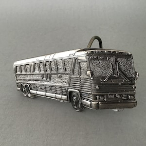 May include: A silver-toned belt buckle shaped like a bus. The bus has a textured surface and says "NEW YORK" on the front.