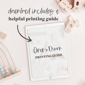May include: A digital tablet shows a printing guide titled "Over the Moon." Wooden toys, including a bead maze and alphabet blocks, surround the tablet. The text "download includes a helpful printing guide" is at the top of the image.