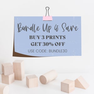 May include: A light blue paper with the text "Bundle Up & Save" and "Buy 3 Prints Get 30% Off" is held by a pink paper clip. The text "Use Code: BUNDLE30" is also visible. Wooden blocks are in the foreground.