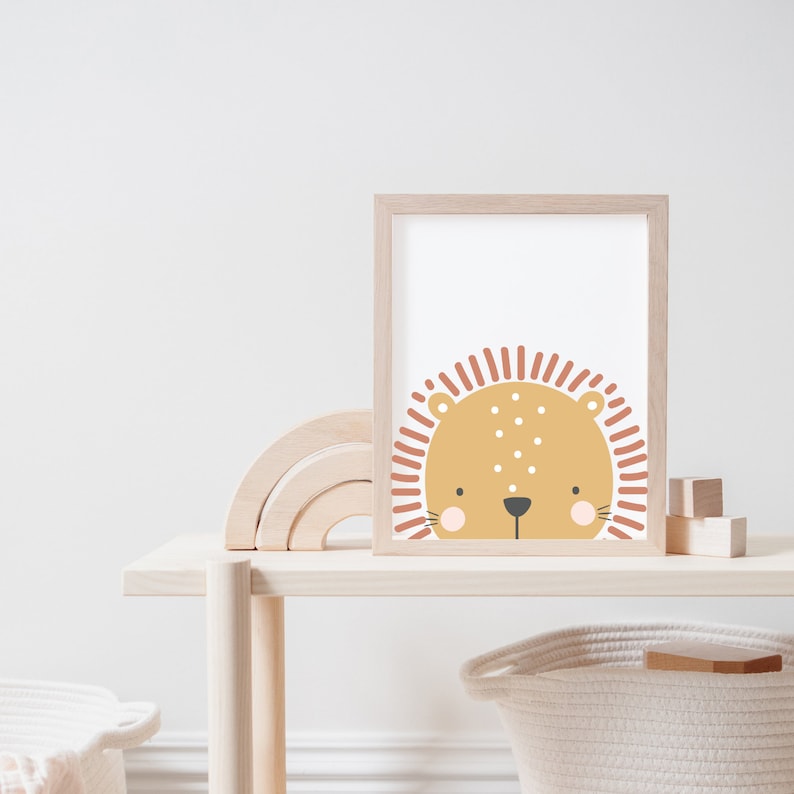 May include: A framed print of a cartoon lion's face in tan, peach, and brown. The artwork is on a light wood shelf with a wooden rainbow and blocks. A woven basket is below. The shelf is made of light wood.
