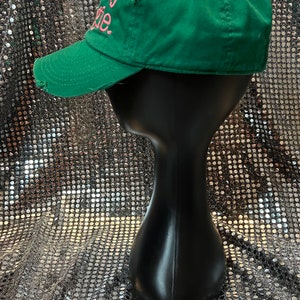 Op de afbeelding: Een groene baseballpet met een roze geborduurde tekst "Really Rosie". De pet heeft een verweerde look met een kleine scheur aan de voorkant.
