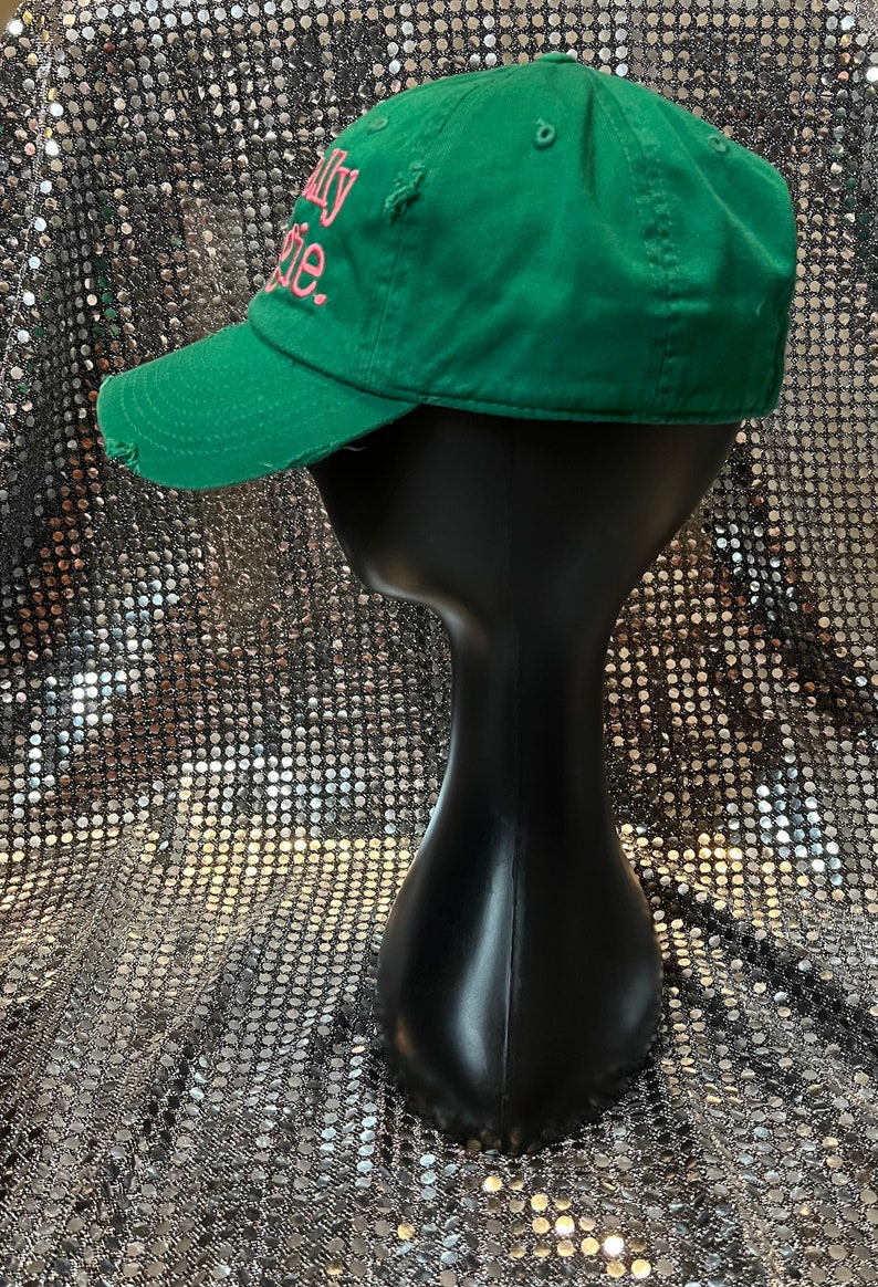 Op de afbeelding: Een groene baseballpet met een roze geborduurde tekst "Really Rosie". De pet heeft een verweerde look met een kleine scheur aan de voorkant.