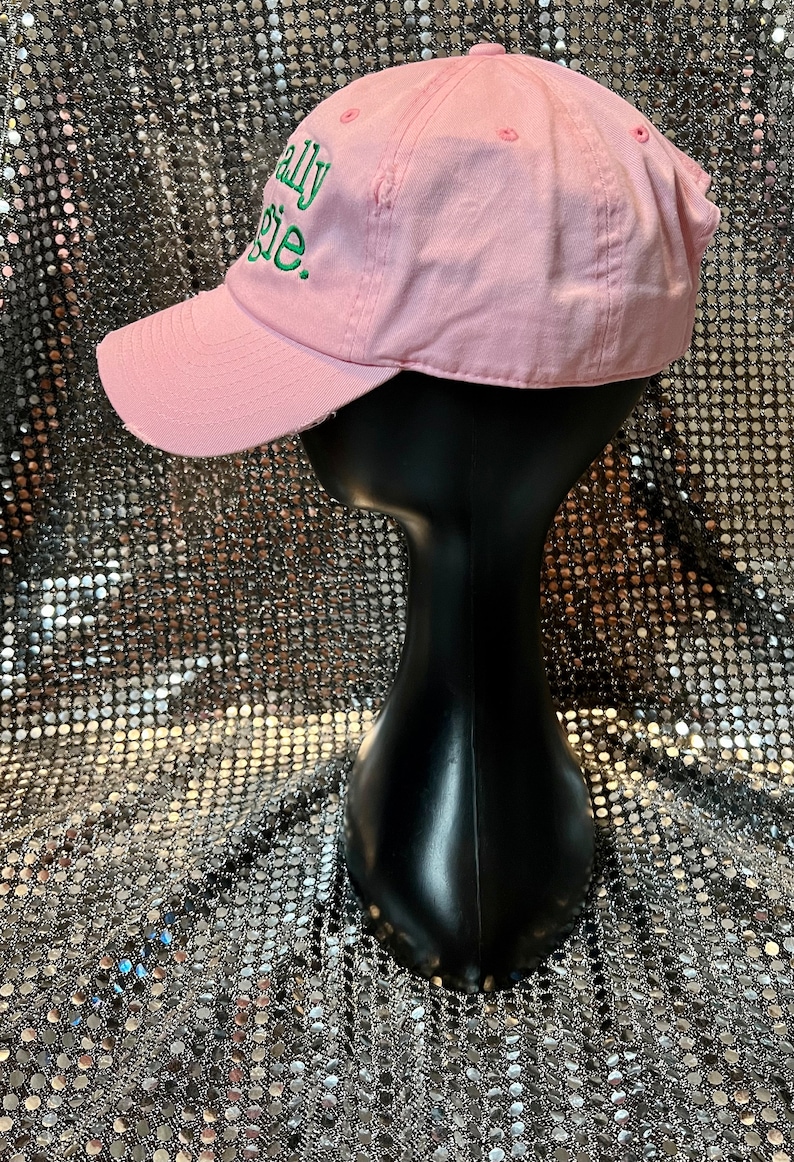 Puede incluir: Gorra de b&eacute;isbol rosa con una frase bordada en verde "Totally Basic" en la parte delantera.