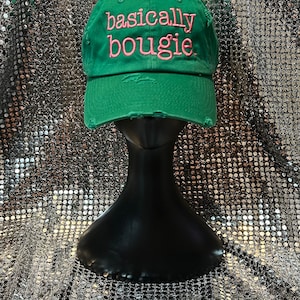 Op de afbeelding: Groene baseballpet met distressed stof en roze geborduurde tekst die "basically bougie" luidt.
