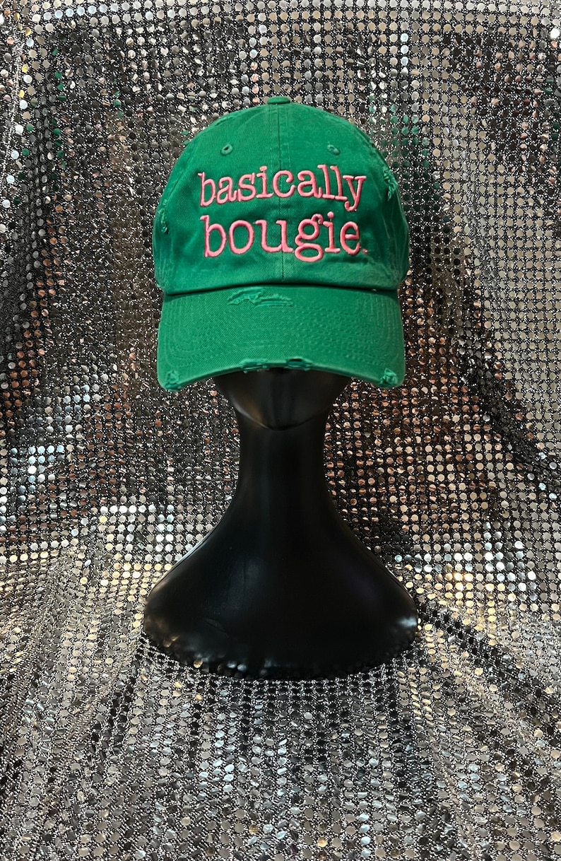 Op de afbeelding: Groene baseballpet met distressed stof en roze geborduurde tekst die "basically bougie" luidt.