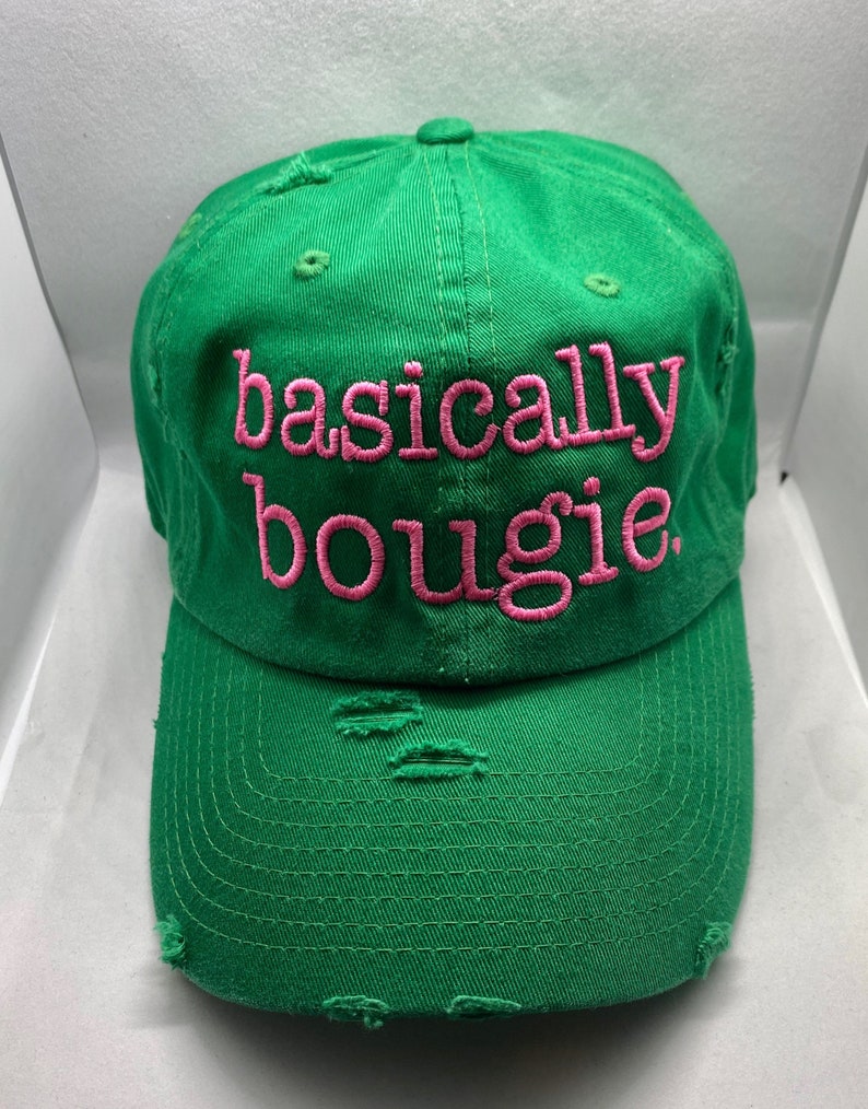 Op de afbeelding: Groene baseballpet met distressed details en roze geborduurde tekst die "basically bougie" luidt.