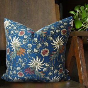May include: A blue cushion with a floral pattern featuring white, orange, and red accents. The cushion is sitting on a wooden chair.