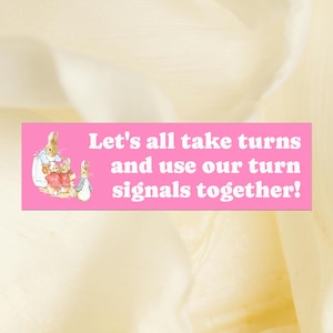 May include: A rectangular pink bumper sticker featuring a classic illustration of three rabbits in blue and red clothing. The white text reads: Let's all take turns and use our turn signals together! The design is centered on a soft, light-colored background.