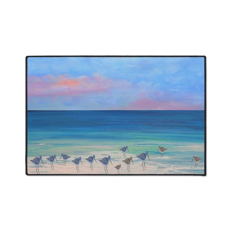 Op de afbeelding: Een rechthoekige bureaumat met een schilderij van een groep kleine strandvogels die op een zandstrand aan de waterkant staan. De sc&egrave;ne bevat een turquoise oceaan, een donkerblauwe horizon en een lucht met zachte roze en blauwe wolken.