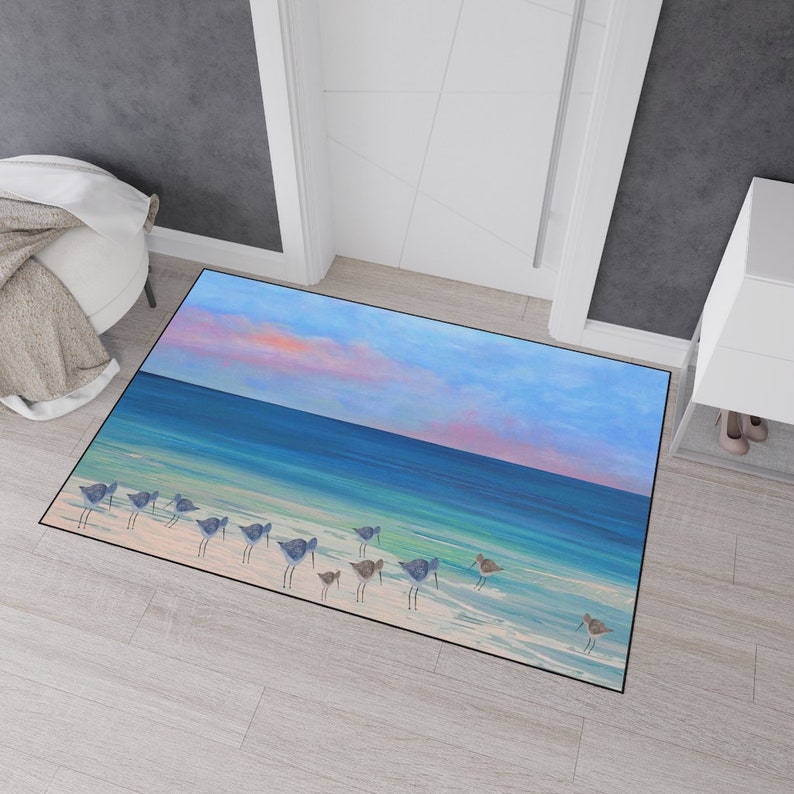 Op de afbeelding: Een rechthoekige deurmat met een bedrukte kustsc&egrave;ne van een groep kleine strandvogels die over een zandstrand lopen. De afbeelding toont een turquoise oceaan, een diepblauwe horizon en een lucht met zachtroze en blauwe wolken bij zonsondergang.