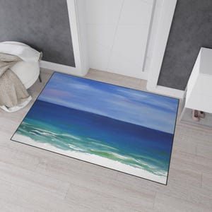 Könnte beinhalten: Eine rechteckige Fußmatte mit einer Ozeanszene. Das Kunstwerk zeigt einen blauen Himmel über einem tiefblauen Meer, das in türkisfarbene und weiße Wellen übergeht. Die Matte hat einen schwarzen Rand und liegt auf einem hellen Holzboden.