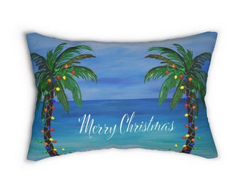 May include: A rectangular pillow with a tropical Christmas theme. Two palm trees are decorated with colorful Christmas lights. The words "Merry Christmas" are written in white script across the bottom, with a blue ocean and sky background.
