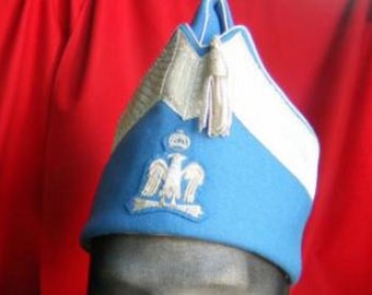 May include: A blue and white military style hat with a silver eagle emblem and a white tassel.