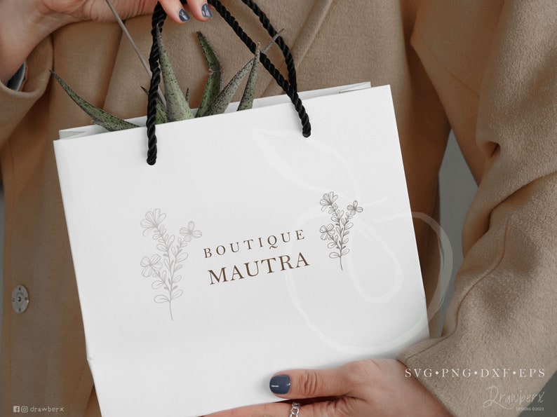 May include: White paper shopping bag with black handles and a logo that says "Boutique Maufra" with a floral design on either side of the text.