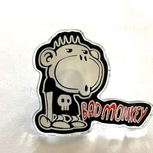 May include: A sticker featuring a cartoon monkey with a black t-shirt and a skull graphic. The monkey has a stern expression and the words "BAD MONKEY" in red and white are below it.