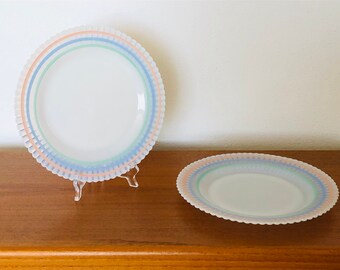 May include: Two white ceramic plates with a scalloped edge and a multi-colored stripe design. The stripes are pink, blue, and green.
