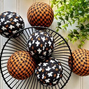 May include: A set of six Halloween-themed fabric balls in a black wire basket. The balls are decorated with black and orange plaid and black with white ghosts and pumpkins.