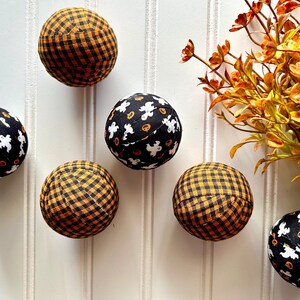 May include: Six Halloween-themed fabric balls. Three are black with white ghosts and orange pumpkins, and three are black and orange gingham.