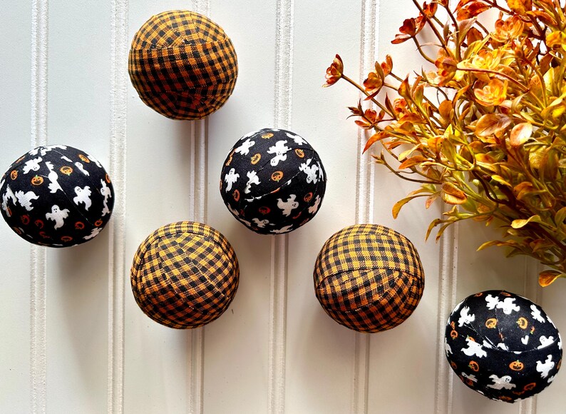 May include: Six Halloween-themed fabric balls. Three are black with white ghosts and orange pumpkins, and three are black and orange gingham.