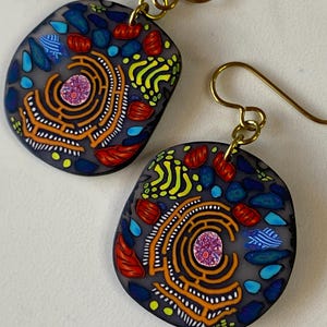 May include: A pair of dangle earrings with a gray background and colorful abstract designs. The earrings are made of polymer clay and have gold-toned hooks.
