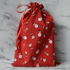 May include: Red fabric gift bag with a drawstring closure and a red ribbon. The bag is decorated with a repeating pattern of snowmen and reindeer.