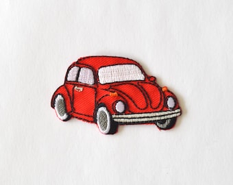 Puede incluir: Un parche bordado con forma de coche antiguo rojo. El diseño presenta ventanas blancas, un parachoques plateado, ruedas negras y blancas, y pequeñas luces de giro naranjas en los guardabarros delanteros, todo delineado en hilo negro.