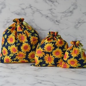 May include: Three reusable shopping bags made of fabric with a sunflower print. The bags are navy blue with yellow and orange sunflowers. The bags are different sizes.
