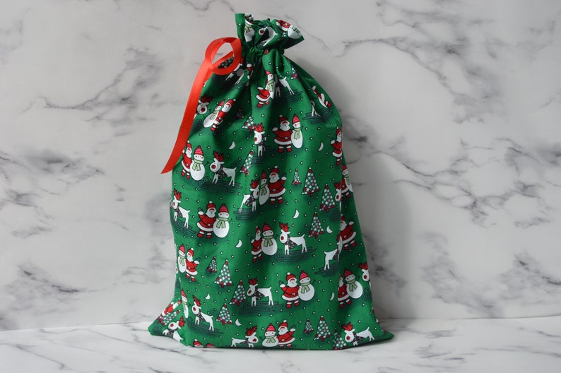 May include: Green fabric gift bag with a drawstring closure and a red ribbon. The bag is decorated with a repeating pattern of snowmen, reindeer, and Christmas trees.