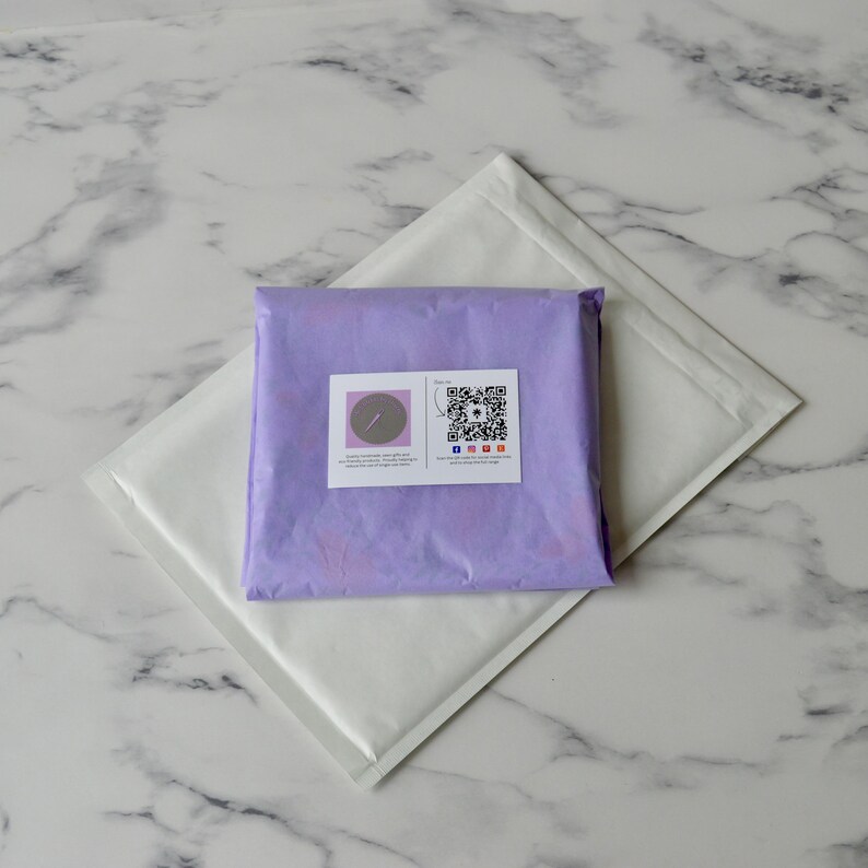 May include: A purple padded envelope with a white label containing a small circle with a needle and thread inside and a QR code with social media icons below it.