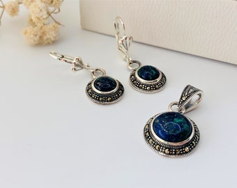 May include: A silver necklace and earrings set with a blue and green gemstone pendant and matching earrings. The pendant and earrings are surrounded by a silver border with small gold accents.