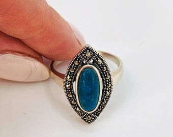 May include: A silver ring with a blue oval gemstone surrounded by a detailed design of marcasite stones.