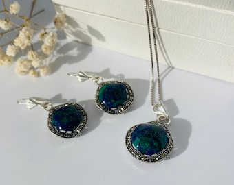 May include: A silver necklace and earrings set with a blue and green gemstone pendant and matching earrings. The pendant and earrings are surrounded by a silver frame with small silver accents.