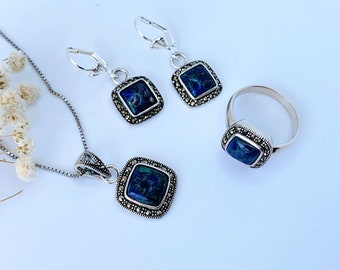 May include: A silver necklace, ring, and earrings set with blue gemstone and marcasite accents. The jewelry features a square-shaped pendant, ring, and earrings.