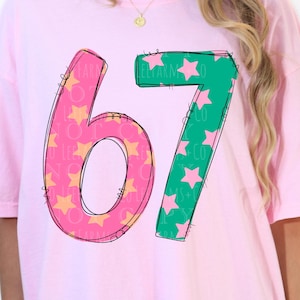 Pu&ograve; includere: T-shirt rosa chiaro oversize con il numero "67" in un design giocoso. Il "6" &egrave; rosa con stelle gialle e il "7" &egrave; verde con stelle rosa. La maglietta presenta anche un logo rotondo con testo ed elementi floreali.