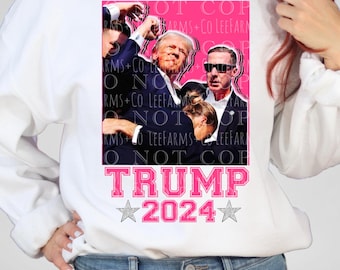 May include: A white sweatshirt with a pink square graphic featuring a group of people. The graphic includes the text "TRUMP 2024" with stars on either side.