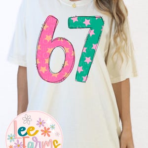 Pu&ograve; includere: T-shirt color crema con il numero "67" in un design giocoso. Il "6" &egrave; rosa con stelle arancioni e il "7" &egrave; verde con stelle rosa. La maglietta presenta anche il logo "Lee Farms + company designs".