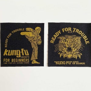 Puede incluir: Dos parches de tela negra con letras doradas. El primer parche presenta una figura de dibujos animados en una pose de karate con el texto "Ready for Trouble kung-fu +Karate for Beginners Home Study Self Defense Course". El segundo parche presenta un tigre con el texto "Ready for Trouble "Kung Fu" +Karate for Beginners".