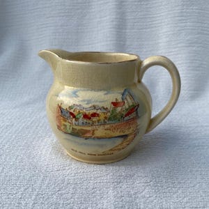May include: A cream-coloured ceramic jug with a handle. The jug has a painted scene of a town with buildings and trees. The text "Old Hill Pond Swansea" is printed on the bottom of the jug.