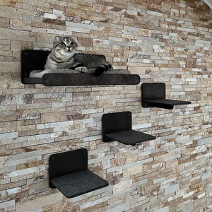 May include: Four black cat shelves mounted on a stone wall. The top shelf has a gray and white cat laying on it.