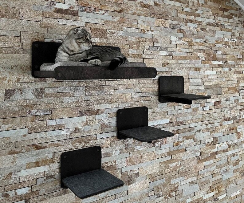 May include: Three black wall-mounted cat shelves with a gray fabric surface. A cat is lying on the top shelf.