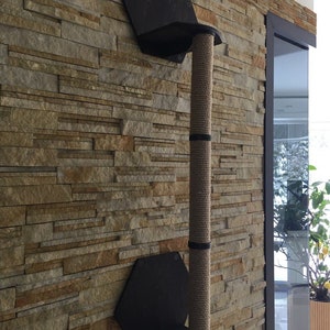 May include: A wall-mounted cat scratching post with a sisal rope covered post and two hexagonal platforms. The post is mounted on a stone wall.