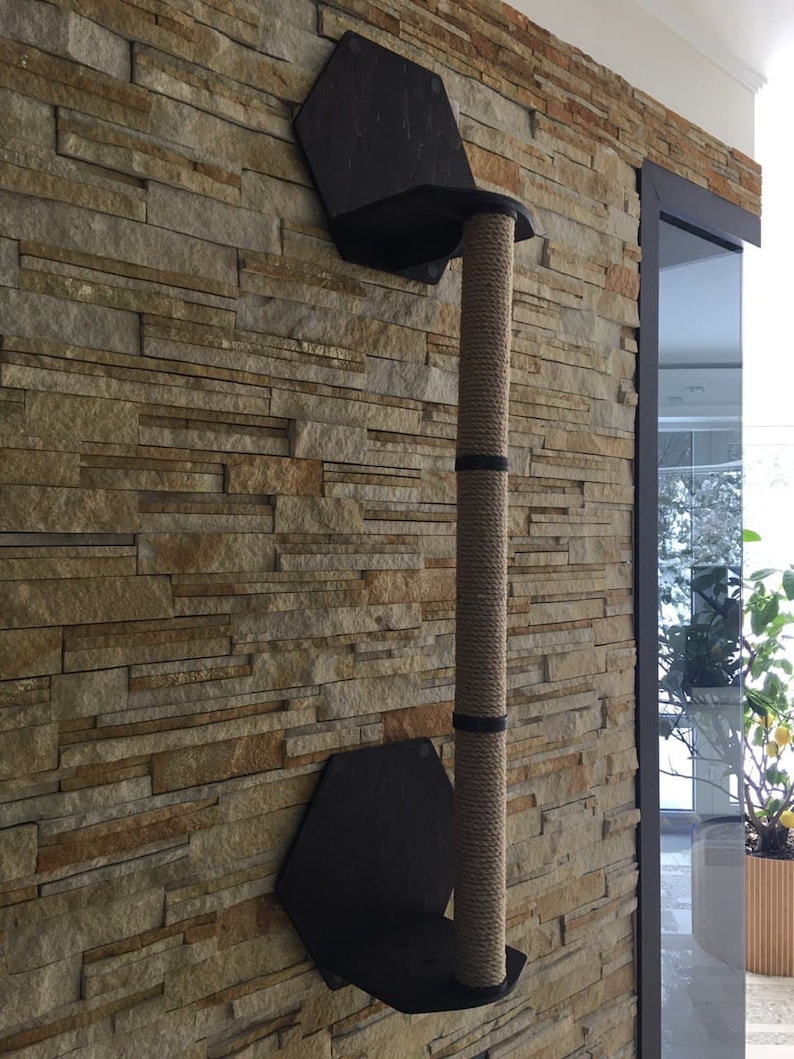 May include: A wall-mounted cat scratching post with a sisal rope covered post and two hexagonal platforms. The post is mounted on a stone wall.