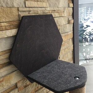May include: A dark brown wooden cat perch with a gray felt platform and a sisal rope post. The perch is mounted to a stone wall.