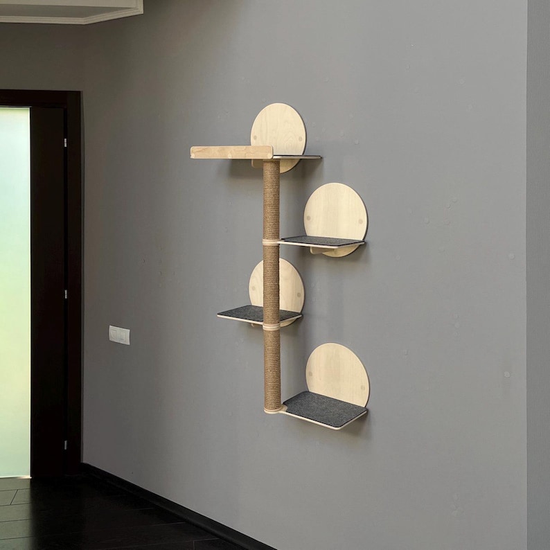 Puede incluir: Un &aacute;rbol para gatos de pared con un poste para rascar cubierto de sisal y m&uacute;ltiples plataformas. Las plataformas son circulares y tienen un acabado en madera clara. Las plataformas est&aacute;n fijadas a la pared con un fondo gris.
