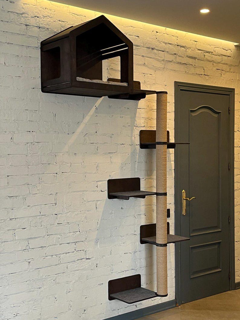 May include: A wall-mounted cat tree with a house, a scratching post, and multiple platforms. The cat tree is made of dark wood and has a natural rope scratching post. The cat tree is mounted on a white brick wall.