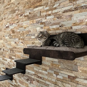 May include: A gray tabby cat with green eyes sits on a black cat tree with a padded platform and steps. The cat tree is mounted on a wall with a stone-like texture.