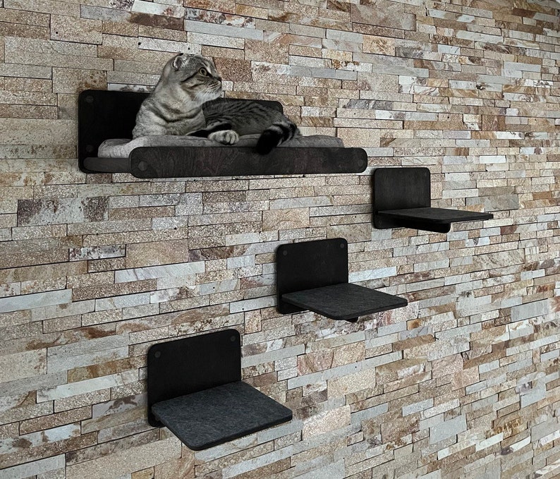 May include: Three black cat shelves mounted on a stone wall. The top shelf has a cat lying on it.
