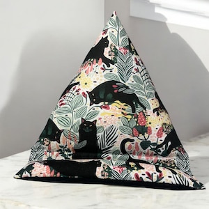 May include: A triangular pillow with a black, white and green fabric featuring a repeating pattern of black cats and flowers. The pillow is designed to prop up a tablet or book.