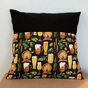 May include: Black and white pillow with a pattern of beer mugs, beer steins, and hops. The pillow has a black fabric top and a white fabric bottom.